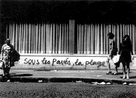 Photo of Paris 1968 street scene with graffiti that reads, "Sous les pavés, la plage